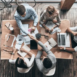 image shot from above of professionals sitting at a table with papers strewn and laptops in use