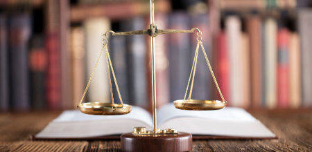 Scales of justice balanced in front of legal books on a shelf.