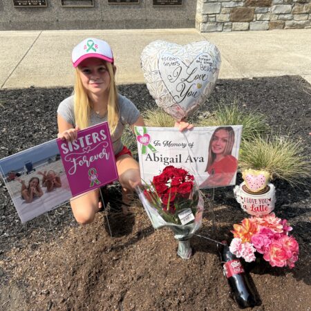 A young girl wearing a baseball cap is pictured next to memorial signs and trinkets.