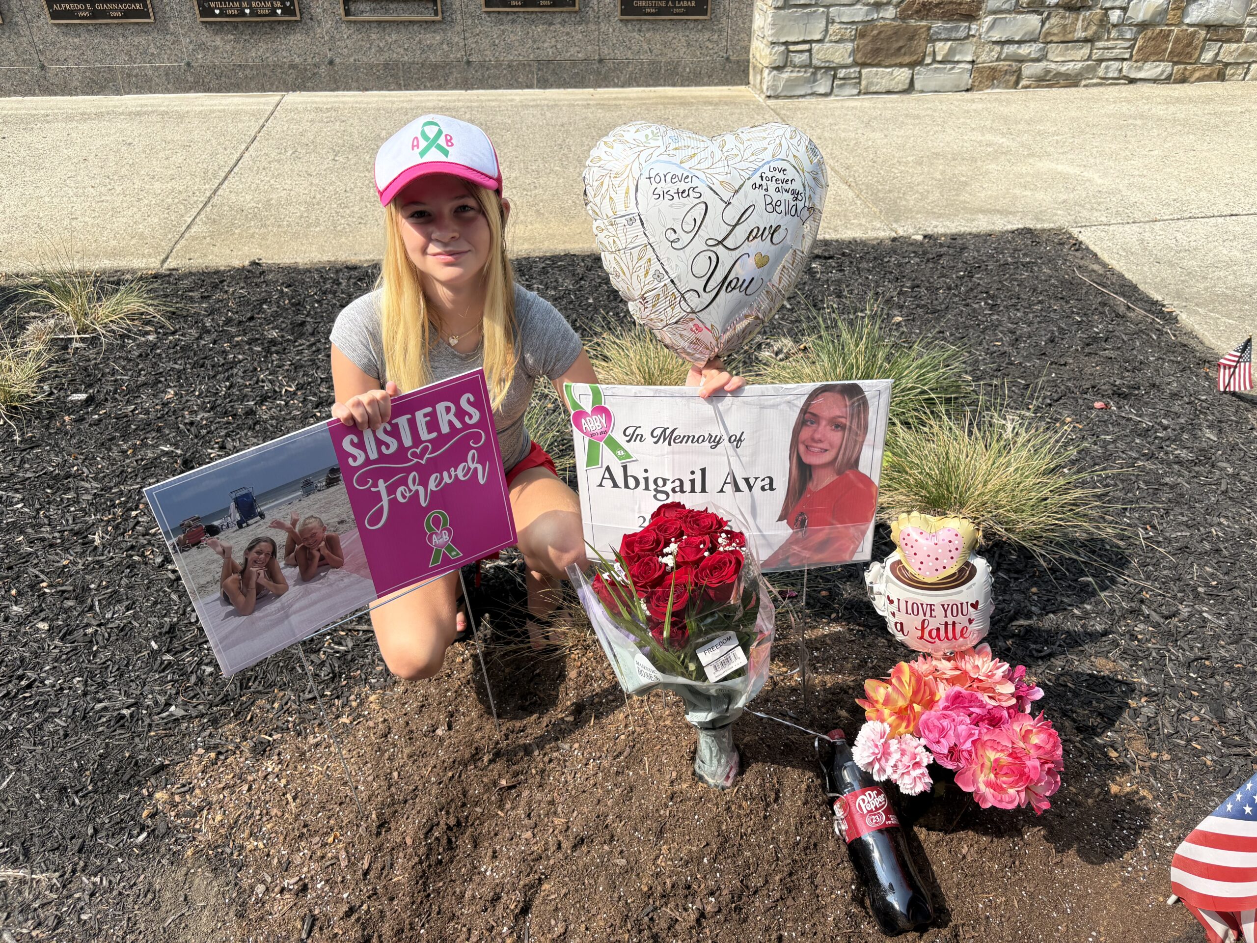 A young girl wearing a baseball cap is pictured next to memorial signs and trinkets.