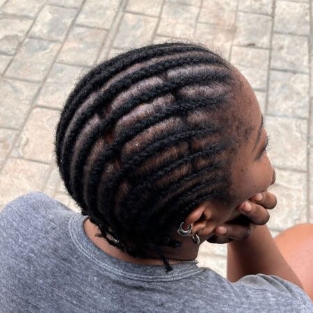 An image of a Black woman, wearing a gray t-shirt, shot from behind. The photo shows the top of her head. Her hair is in braids and she has a scar from a childhood TBI.