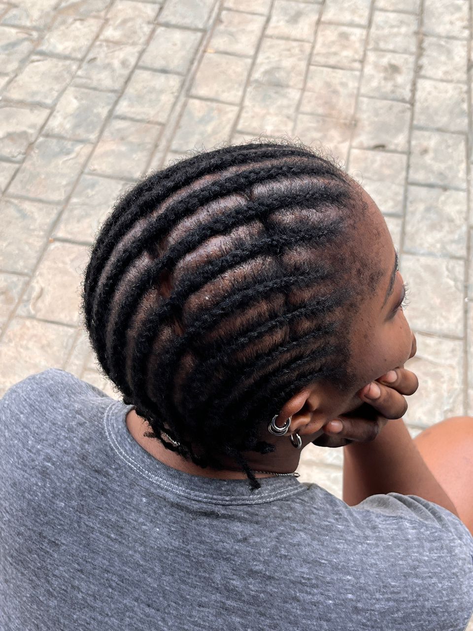 An image of a Black woman, wearing a gray t-shirt, shot from behind. The photo shows the top of her head. Her hair is in braids and she has a scar from a childhood TBI.