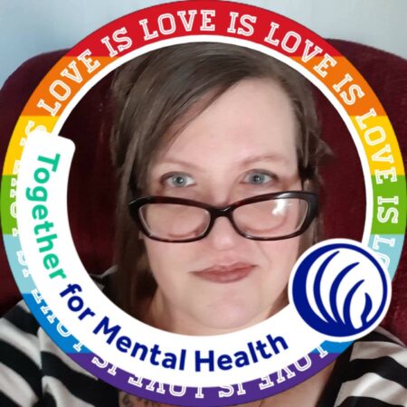 A woman with brown hair, blue eyes, and glasses, is giving a slight smile.