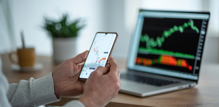 person monitoring stocks on a computer and a phone